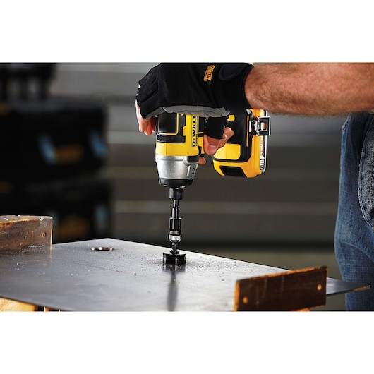 A person wearing gloves uses a yellow and black DEWALT cordless drill to drill a hole into a metal sheet.