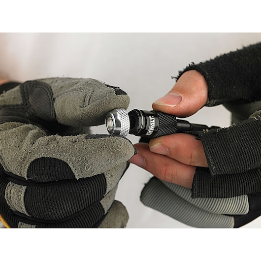 Close-up of gloved hands holding a DEWALT DT71514 screwdriver bit holder.