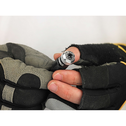 A close-up image of gloved hands holding a DEWALT drill bit holder, with visible wear on the gloves and bits.