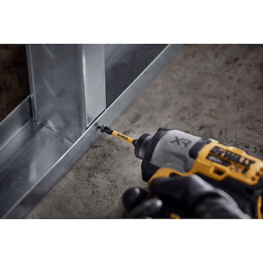 DEWALT drill driving a screw into a metal frame, close-up of tool in use on construction material.