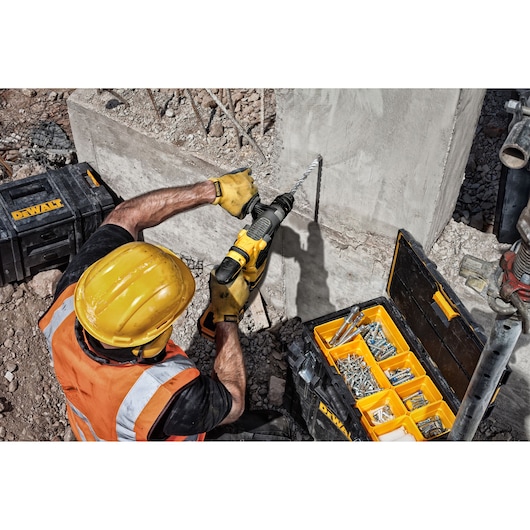 Worker drills concrete wall with DEWALT tool. DT9580, DT9580-QZ SKU cases visible with screws on ground.