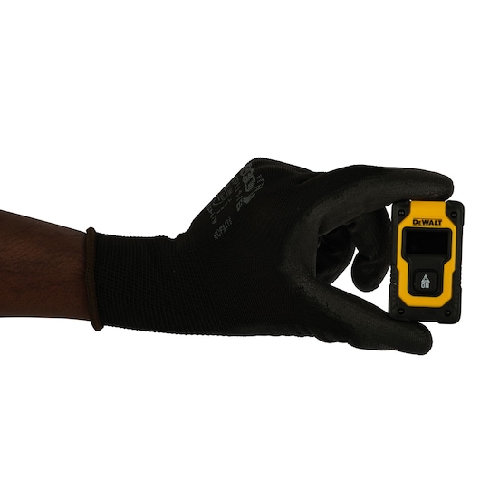 A hand wearing a black glove holding a small yellow and black DEWALT laser distance measurer.