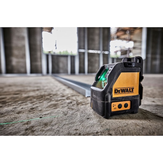 DEWALT green laser level DW088CG on a concrete floor inside a construction site, projecting a straight green line.