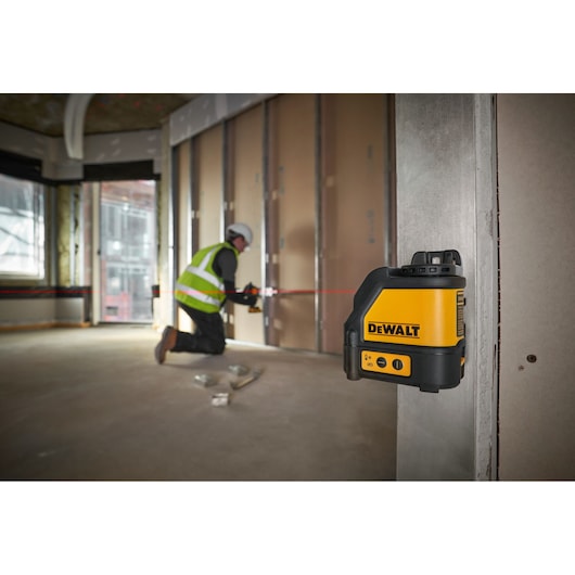 A DEWALT DW088K laser level device is mounted on a metal frame inside a construction site, with building materials and structural elements visible in the background.
