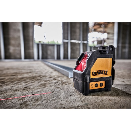 A DEWALT DW088K self-leveling cross line laser level placed on a construction site floor, projecting a visible red laser line used for alignment tasks.