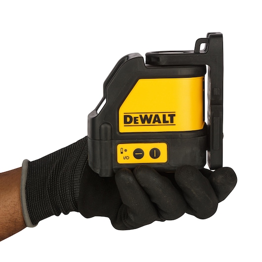 A hand wearing a black glove is holding a DEWALT DW088K self-leveling cross line laser tool. The device is yellow and black with control buttons visible on the front side.