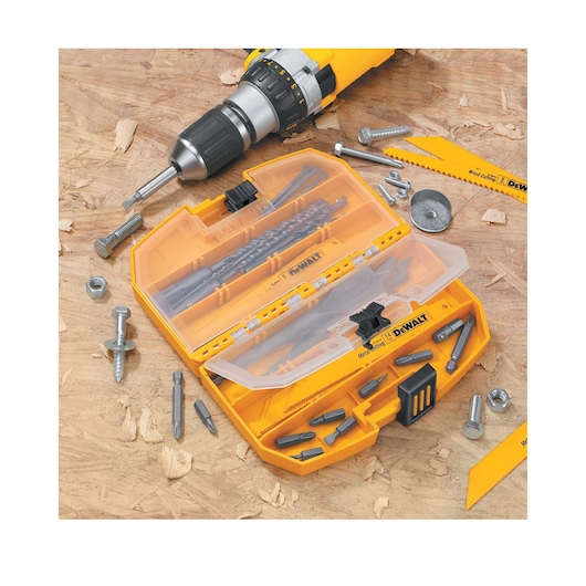A DEWALT branded yellow drill bit and screwdriver bit set in a plastic case is displayed on a wooden surface. The open case contains various bits and accessories, with bolts, screws, and a drill partially visible nearby.