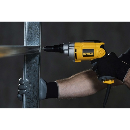 A person wearing protective gloves uses a yellow DEWALT electric screwdriver (model DW268) to drive a screw into a metal beam.