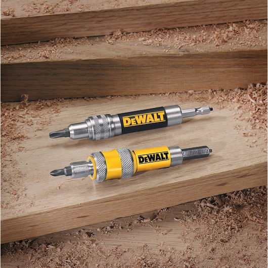 Two DEWALT screwdriver bit holders with quick-change features are placed on a wooden surface with wood shavings around them.