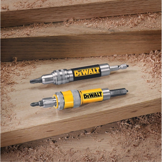 Two DEWALT screwdriver bit holders are displayed on a wooden surface with wood shavings around. The tools have metal bodies with black and yellow DEWALT branding, and are designed for use with power drills.