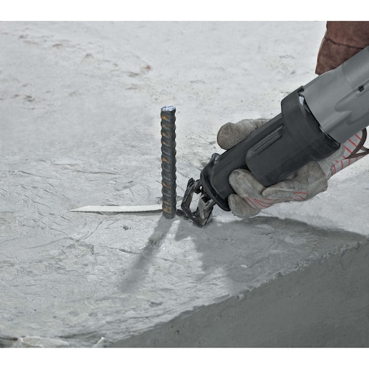 A gloved hand using a DEWALT reciprocating saw to cut through a metal rebar embedded in a concrete surface.