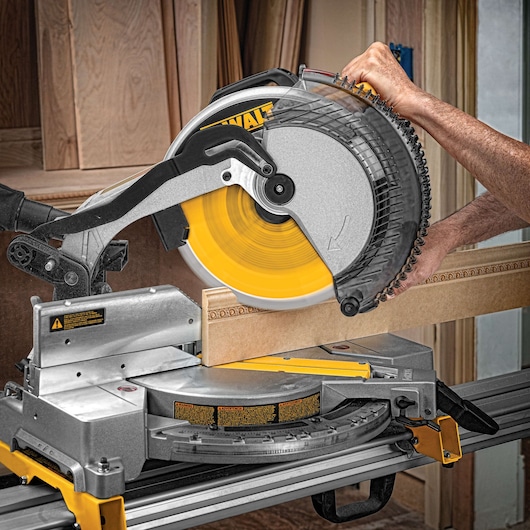 A DEWALT miter saw being used to cut a piece of wood, with a person operating the saw in a workshop setting.