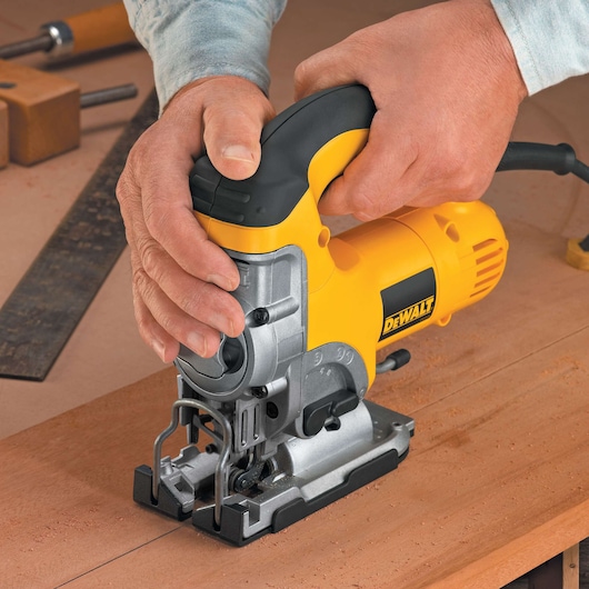 A close-up view of hands operating a yellow DEWALT DW331K jigsaw on a wooden surface.