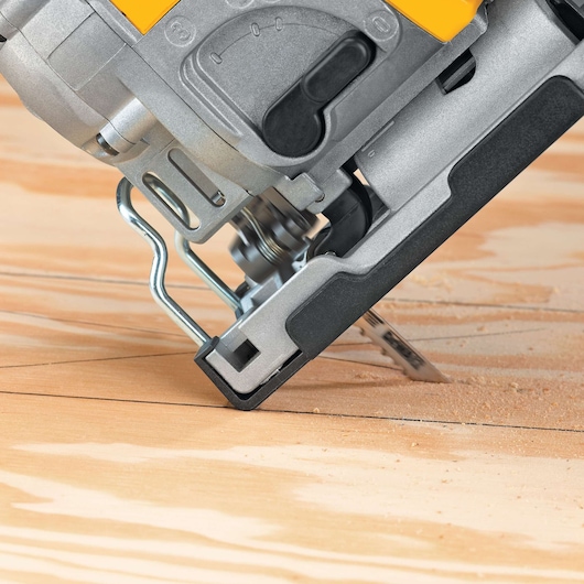 Close-up of a DEWALT jigsaw cutting a wooden surface at an angle, with sawdust visible around the cutting area.