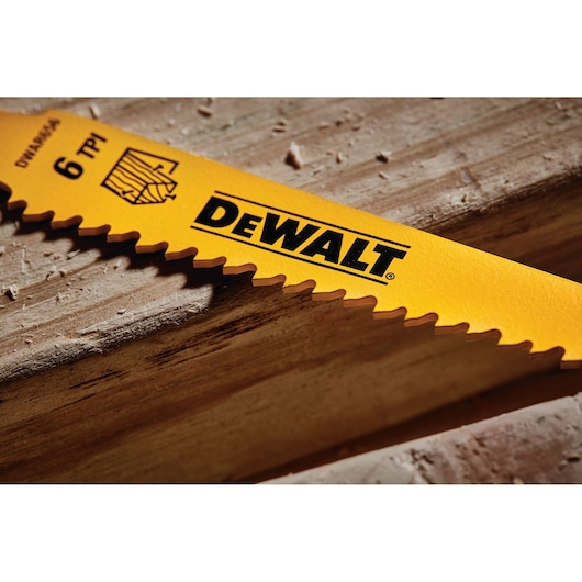 Close-up of a yellow DEWALT saw blade with sharp teeth, placed on a wooden surface. The blade features the DEWALT logo and specifications such as 6 TPI.
