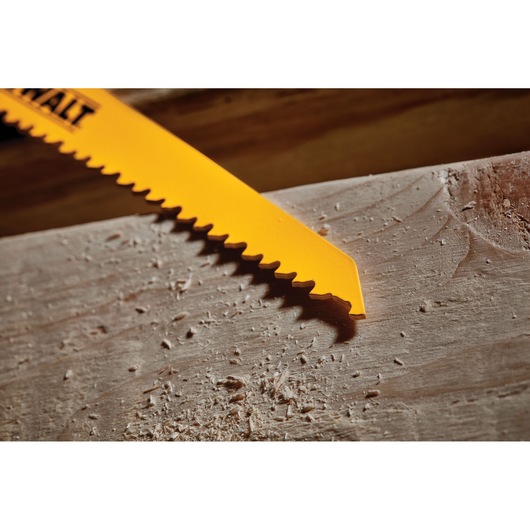 Close-up of a yellow DEWALT saw blade cutting a piece of wood, with wood shavings scattered around.