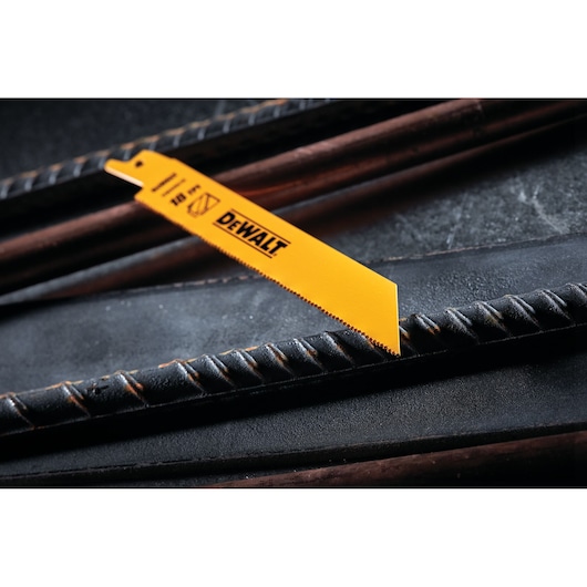 A close-up of a DEWALT DW4811 yellow reciprocating saw blade positioned across metal rebar on a dark surface.