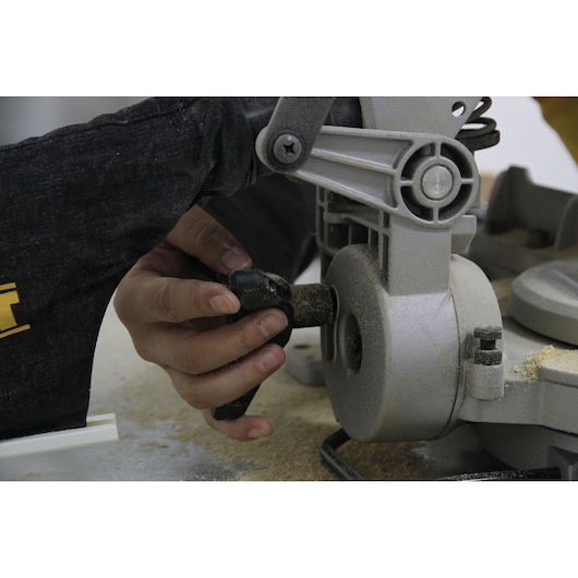 Close-up of a person adjusting the handle of a DEWALT DW714 miter saw, with visible sawdust and part of the saw's mechanism.