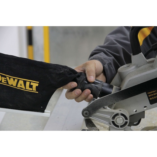 A person is attaching a black dust bag with the DEWALT logo to a DEWALT miter saw.