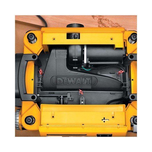 Top view of a DEWALT DW735 wood planer in yellow and black, showing its internal components and mechanical details. The DEWALT logo is visible on the central black cover, and the tool is positioned on a wooden surface.
