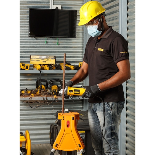 Photo of DEWALT DW802 grinder in use cutting metal rod, worker with safety gear in workshop setting.