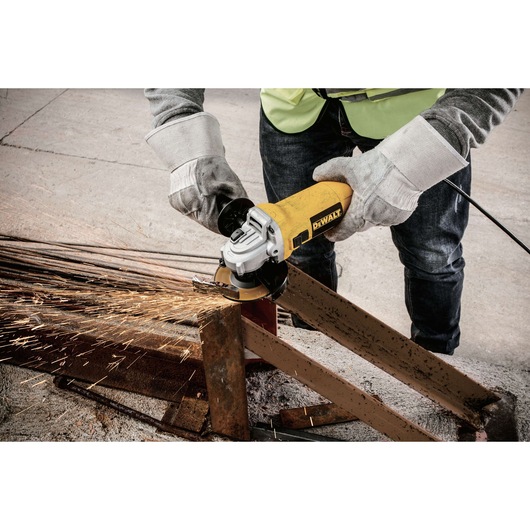 A worker wearing protective gloves and sleeves is using a yellow DEWALT angle grinder to cut through a metal beam, with sparks flying from the cutting area.