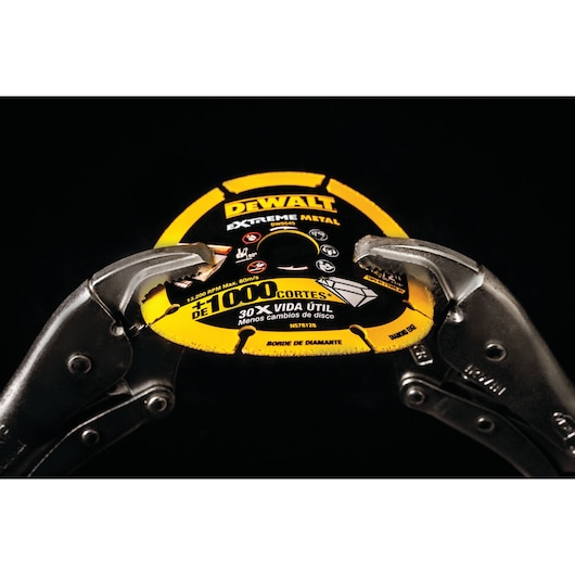Close-up of a DEWALT Extreme Metal cutting disc, gripped by two metal locking pliers against a black background. The yellow and black disc highlights its durability and performance specifications for metal cutting.
