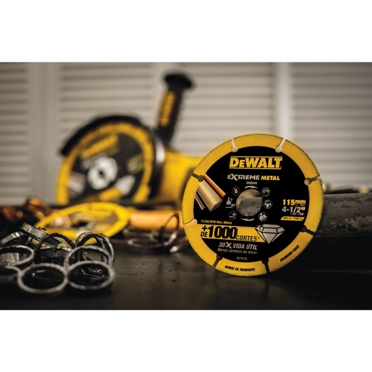 A close-up of a DEWALT Extreme Metal cutting disc, model DW8545, with a size of 115 mm (4-1/2 inches), placed on a workbench. Several metal rings and another tool are blurred in the background.