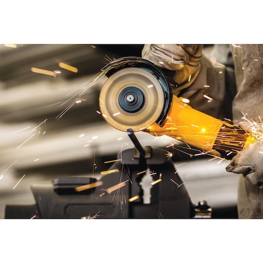 A close-up of a person using a yellow angle grinder to cut metal, with sparks flying.
