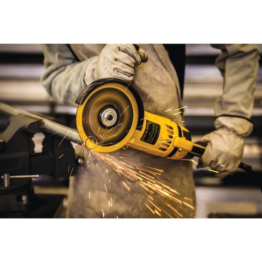 A person wearing protective gloves uses a yellow DEWALT angle grinder to cut a metal pipe, with sparks flying from the cutting area.