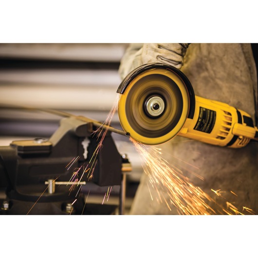 A close-up view of a person using a yellow DEWALT angle grinder to cut metal, with bright sparks flying from the cutting area. The person is wearing protective gloves.
