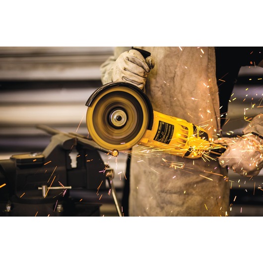 A person wearing gloves and protective clothing uses a yellow DEWALT angle grinder to cut metal, creating sparks.