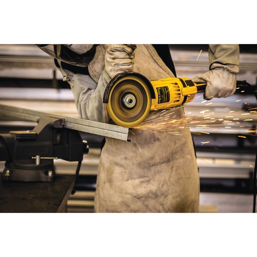 A person wearing protective gloves and apron uses a yellow DEWALT angle grinder to cut a metal piece, creating sparks.