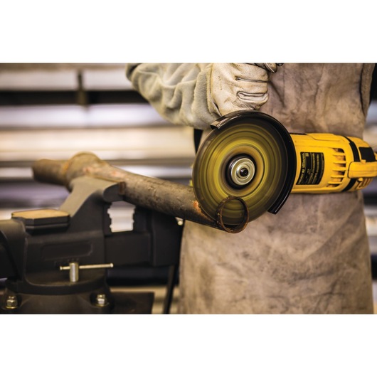 A person wearing protective gloves and apron uses a yellow DEWALT angle grinder to cut through a metal pipe secured in a vise.