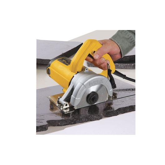 A close-up of a person using a yellow DEWALT DW862 electric circular saw to cut a piece of stone or tile.