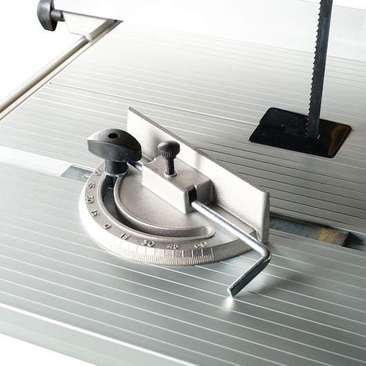 Close-up of an adjustable metal miter gauge attached to a table saw, with a vertical saw blade partially visible in the background.