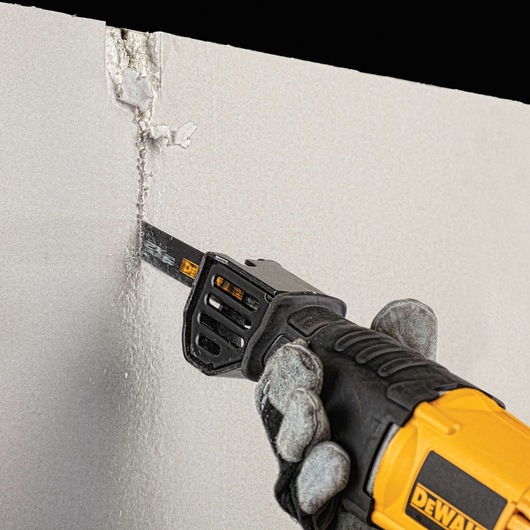 A close-up of a gloved hand using a DEWALT reciprocating saw to cut through a sheet of drywall.