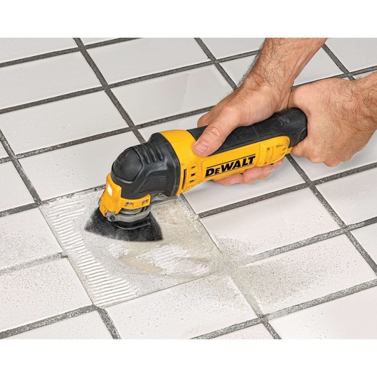 A DEWALT oscillating multi-tool being used to remove grout from between white ceramic tiles.