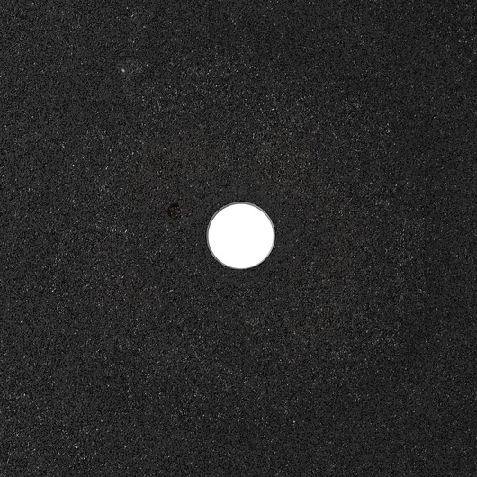 A close-up view of a DEWALT abrasive disc with a central circular hole, showing a rough black textured surface.