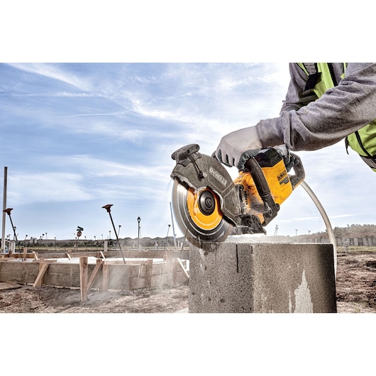 A person wearing gloves uses a DEWALT power saw to cut through a concrete block at a construction site under a clear sky.
