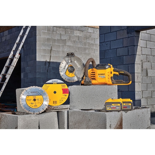 A DEWALT cordless power tool with multiple cutting blades and two FLEXVOLT batteries displayed on concrete blocks at a construction site. A ladder and cinder block walls are visible in the background.