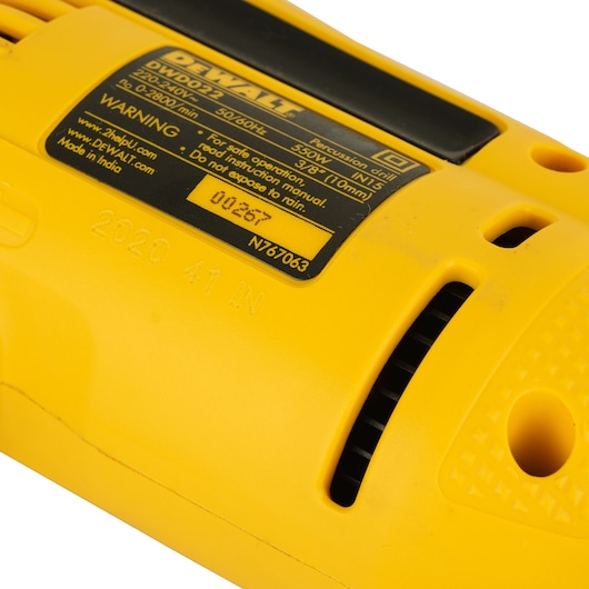 Close-up image of the yellow casing of a DEWALT percussion drill with visible product label showing specifications such as model DWD022, voltage, and operational warnings. The air vents and part of the handle are also shown.