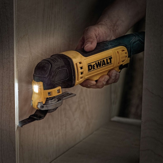 A hand using a DEWALT DWE315 multi-tool with a built-in LED light to cut into a piece of wood.