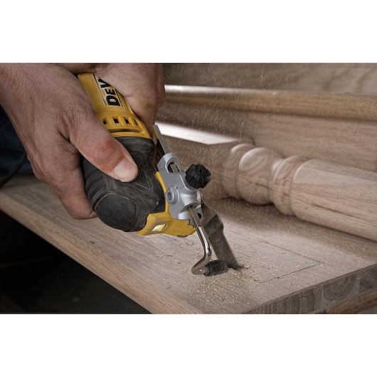 A close-up of a person using a yellow DEWALT oscillating multi-tool to cut into a piece of wood, with sawdust flying.
