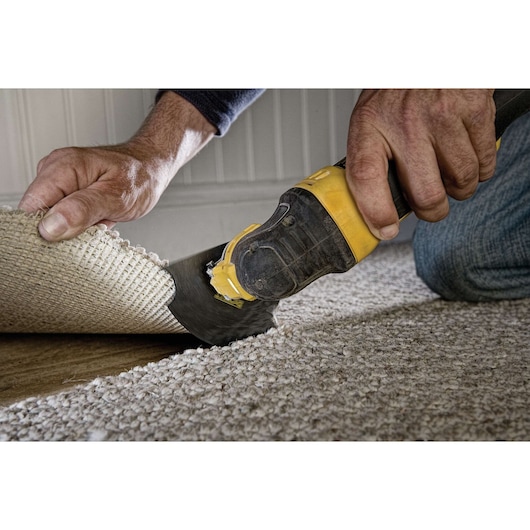A close-up of a person using a DEWALT oscillating multi-tool to cut carpeting near the edge of a room.