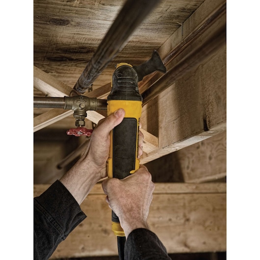 Hands using a DEWALT DWE315 oscillating multi-tool to cut a pipe under wooden beams.