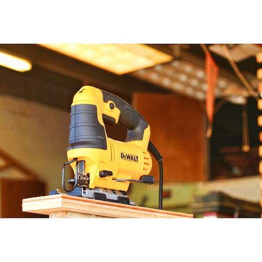 A DEWALT DWE349 jigsaw power tool is placed on a wooden board in a workshop environment.