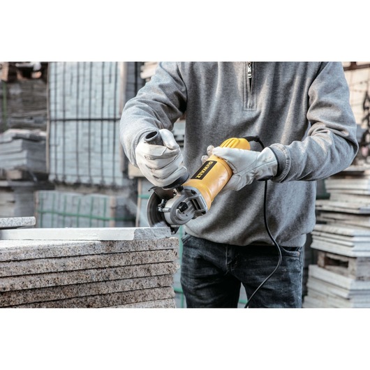 A person wearing gloves is using a yellow DEWALT angle grinder to cut stone slabs in an industrial or construction setting.