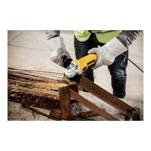 A person wearing safety gloves uses a DEWALT DWE4010 angle grinder to cut a metal beam, with sparks flying from the grinding area.