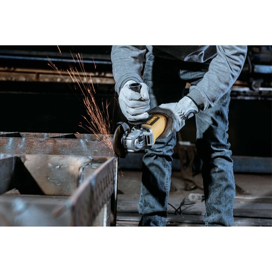 A person wearing gloves and jeans is using a yellow DEWALT angle grinder, generating sparks while cutting or grinding a metal surface in a workshop environment.